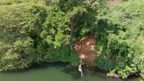 Aerial-shot-of-African-boy-on-a-rope-swing-on-the-banks-of-the-river-Nile-doing-a-back-flip-into-the-water