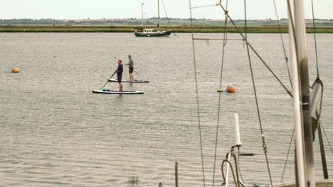 Footage-showing-two-men-standup-paddle-boarding-across-the-frame,-this-is-filmed-at-Heybridge-basin-in-Essex