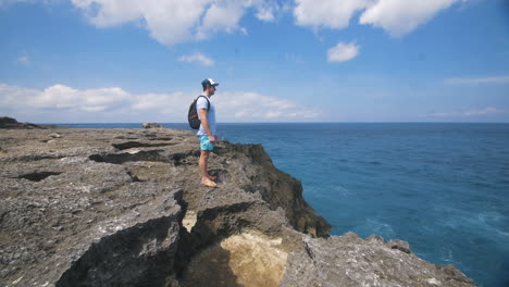 Traveling-Man-Standing-on-Edge-of-Rocks-Looking-Out-at-Ocean---Pan-Up-Reveal