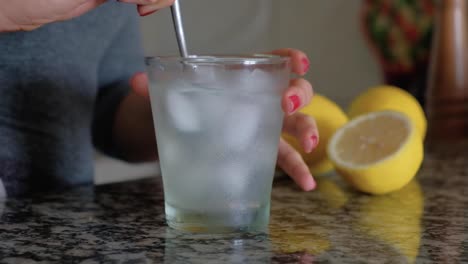 Woman-stirring-with-a-spoon-a-glass-with-lemonade-and-ice-cubes