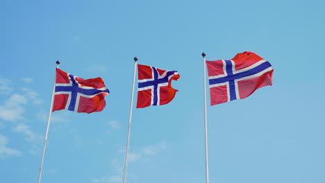 Three-Norwegian-flags-fluttering-in-the-wind-in-slowmotion-with-blue-sky-in-the-background