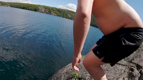 Jump-Off-Tall-Cliff-with-Young-White-Male-into-Blue-Lake,-POV-Slow-Motion-Wide-Action-Tracking
