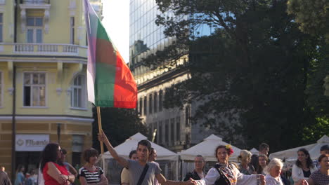 Bulgarien:-Ein-Mann-Schwenkt-Stolz-Die-Bulgarische-Nationalflagge,-Während-Menschen-Auf-Einem-öffentlichen-Platz-In-Sofia-Tanzen