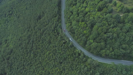Silver-car-and-red-SUV-driving-on-curvy-mountain-road-with-deep-forest-from-both-sides-of-the-road