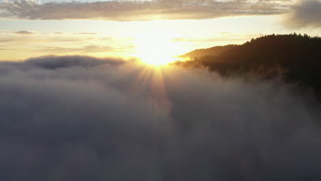 Aerial-drone-footage-of-sunrays-peaking-over-magical-fog-and-mountain-tops-at-sunset