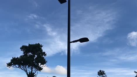 Upward-pan-of-a-street-light-with-two-lamps-in-silhouette-against-a-blue-sky-with-wispy-clouds