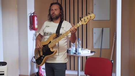 Man-playing-bass-guitar-in-recording-studio,-medium-shot