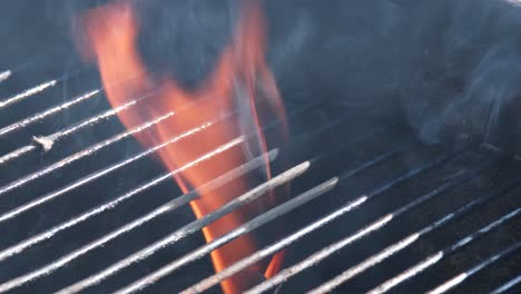 An-open-flame-leaping-through-the-grid-when-preparing-a-barbecue,-close-up