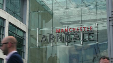 Arndale-Shopping-Centre-Manchester-City-Centre-close-up-of-the-sign-on-summer-sunny-day-with-people-passing-in-front-close-up-4K-25p