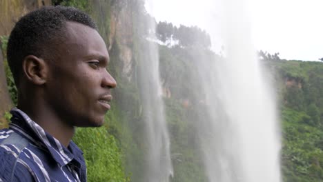 Close-up-slow-motion-shot-of-a-young-African-mans-face-as-he-looks-out-behind-a-tropical-waterfall