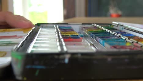 Close-up-of-artist-mixing-watercolors-and-making-circles-on-a-painting-palette