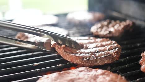 Slow-motion-extreme-close-up-of-steaming,-juicy-burger-being-flipped-by-tongs-on-a-fire-grill