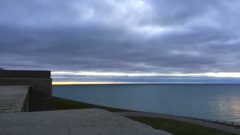 Time-lapse-of-early-morning-on-Lake-Ontario,-shot-from-hilltop-rampart,-showing-wave-patterns,-cloud-movement-and-people-out-for-a-walk