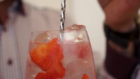Slowmo---Männlicher-Barmann,-Der-Einen-Gin-Tonic-Drink-Cocktail-Mit-Erdbeeren-Und-Eiswürfeln-Im-Glas-Zubereitet---Nahaufnahme