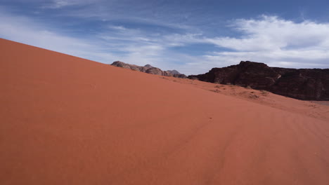 Walking-Downhill-From-The-Sand-Dune-With-Mountains-and-Sand-Grass-Visible-in-the-Background