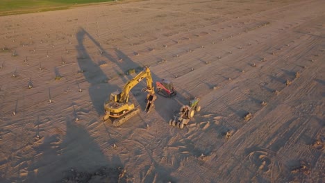 Aerial-shot-of-a-backhoe-and-a-forklift-parked-in-an-empty-field-during-golden-hour