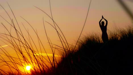 Silhouette-of-woman-standing-on-dune-in-Vrksasana---tree-asana-in-rays-of-sunset