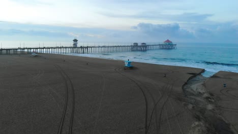 Bei-Sonnenaufgang-über-Den-Sand-Zum-Huntington-Beach-Pier-In-Der-Surf-City-In-Kalifornien-Gleiten,-Während-Die-Menschen-Ihren-Urlaub-Genießen-Und-Surfer-Wellen-Fangen