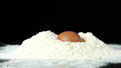 Whole-Egg-Dropping-into-Flour,-Against-a-Black-Background