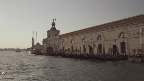 Wide-shot-of-Gondolas-in-front-of-Punta-della-Dogana,-Museum-of-art-on-a-beautiful-sunny-morning,-Venice,-Italy
