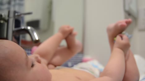 Cute-six-months-old-baby-boy-playing-with-dummy-and-his-feet-in-the-bathroom