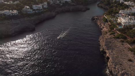 AERIAL:-Following-a-Boat-driving-out-Bay-of-Cala-D'or-in-Mallorca,-Spain