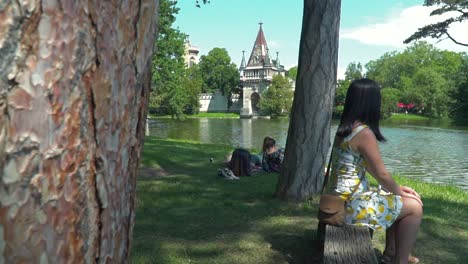 Slide-reveal-of-girl-in-summer-dress-sitting-on-park-bench-with-backdrop-of-Laxenburg-Castle-near-Vienna