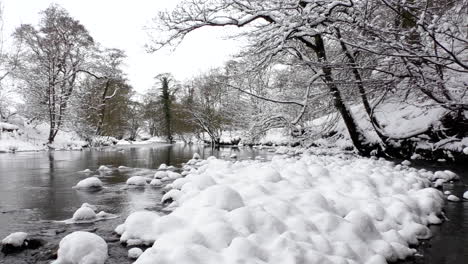 Looking-upstream-a-river-with-snow-covered-rocks-and-trees