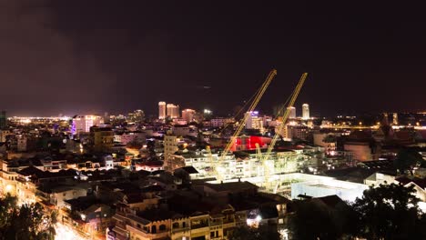 Phnom-Penh-Cityscape-at-night---cranes-in-foreground,-zoom-in
