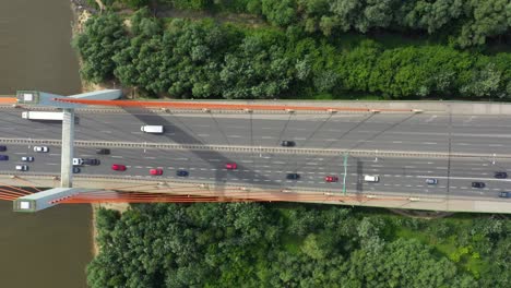 City-car-moving-at-highway-bridge-on-background-smooth-river-surface-drone-view