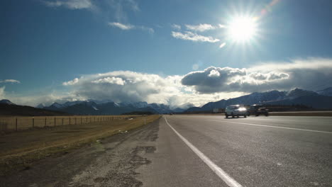 Wide-angle-of-vehicles-driving-down-highway-with-beautiful-mountains-and-clouds-in-the-background-as-the-sun-shines-overhead