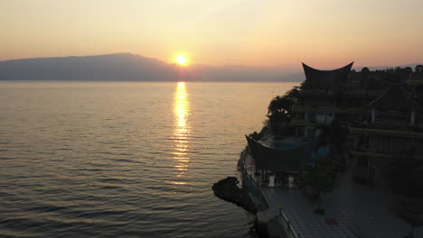 Drone-flyover-of-waterfront-resorts-on-Samosir-Island-on-Lake-Toba-in-North-Sumatra,-Indonesia-at-sunrise