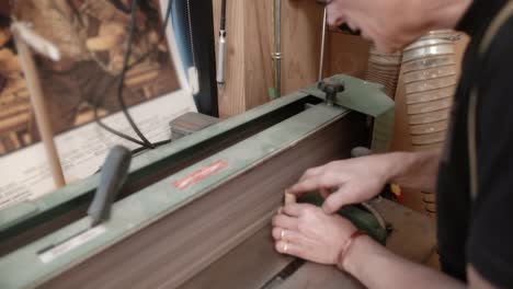 Woodworker-using-industrial-belt-sander-to-smooth-circular-wood-piece