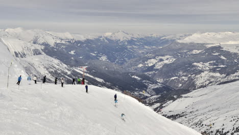 Time-lapse-of-skiers-,-skiing-down-a-slope-piste-in-French-Alps-with-snowy-valley-behind