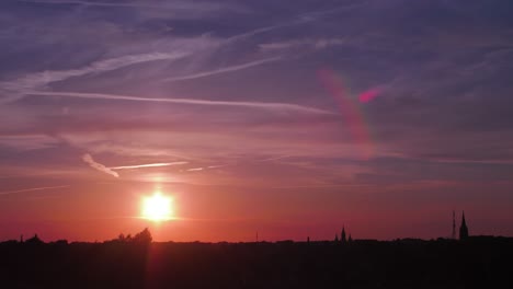 Time-lapse-of-beautiful-scenic-red-sunset-over-the-city-with-sun-shining-through-the-clouds-with-sun-flare,-wide-shot