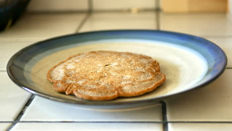 Placing-a-hot-whole-wheat-pancake-from-the-pan-onto-a-plate-during-breakfast-in-kitchen