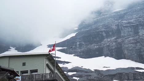 Bandera-Suiza-Ondeando-Dramáticamente-Con-Pájaros-Volando-En-Cámara-Lenta-En-Las-Montañas-Eigergletscher