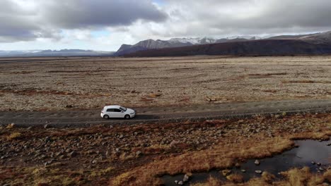 Wide-Profile-Shot-of-a-Car-Driving-Along-a-Dirt-Road-in-Iceland