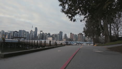 Wide-backward-moving-shot-of-a-Stanley-park-trail-and-Morning-Vancouver-downtown,-Slowmotion