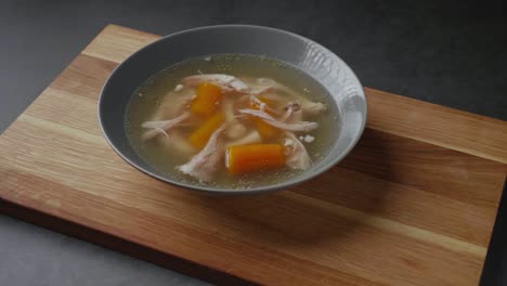 Serving-fresh-hot-healthy-paleo-chicken-broth-soup-to-wooden-board-on-concrete-background