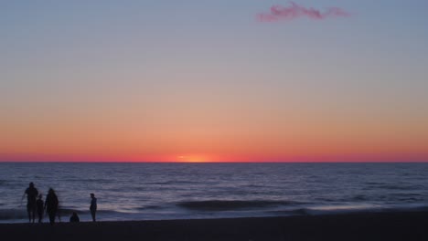 Time-lapse-of-beautiful-scenic-beach-view-at-sunset-with-silhouettes-of-people-at-the-seaside,-wide-shot