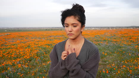 A-pretty-young-woman-showing-sad-and-grieving-emotions-on-her-face-in-a-field-of-wild-flowers-in-nature-SLOW-MOTION