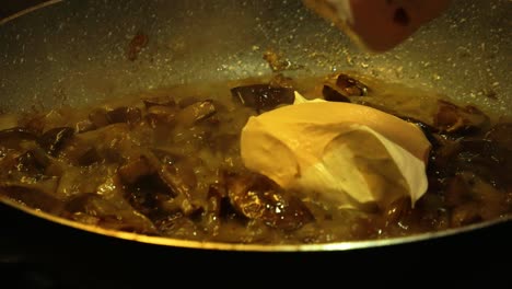 Pouring-sour-cream-to-the-pan-full-of-frying-mushrooms-and-mixing-it