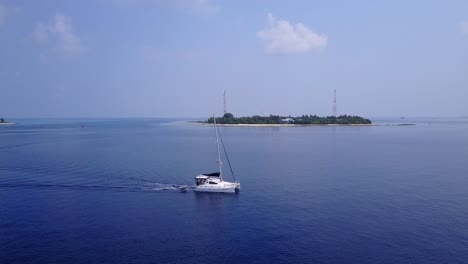 Yacht-sailing-slowly-around-tropical-islands-on-calm-blue-sea-at-sunrise-with-misty-sky-in-beautiful-seascape-of-Maldives