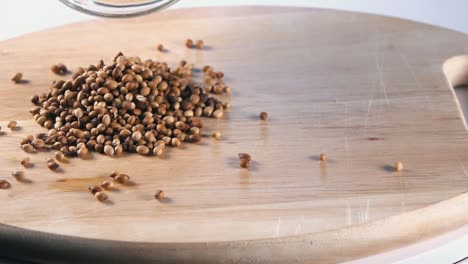 Slow-Motion-Shot-of-Coriander-Seeds-Being-Poured-on-to-a-Wooden-Board