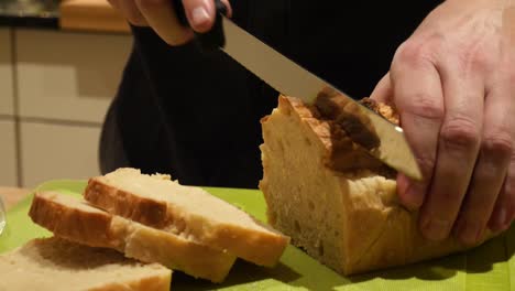A-white-male-hand-model-is-slicing-fresh-baked-toast-bread-on-a-green-cutting-board