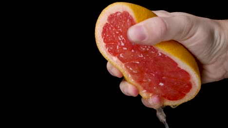 Slow-motion-squeezing-a-half-cut-grapefruit-with-a-white-hand-with-a-lot-of-pressure-on-a-black-background