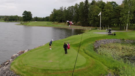 Luftbogenaufnahme-Eines-Golfspielers-Und-Caddies-Auf-Einem-Wunderschönen-Golfplatz-Mit-Einem-See-Im-Hintergrund