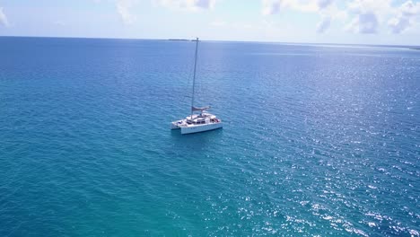 White-catamaran-anchoring-on-blue-azure-calm-waters-next-to-tropical-island-with-resorts-and-villas-inside-lush-vegetation-in-Caribbean