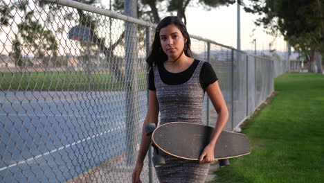 Eine-Süße-Junge-Hispanische-Frau,-Die-Mit-Ihrem-Skateboard-In-Zeitlupe-Durch-Einen-Städtischen-Stadtpark-Läuft